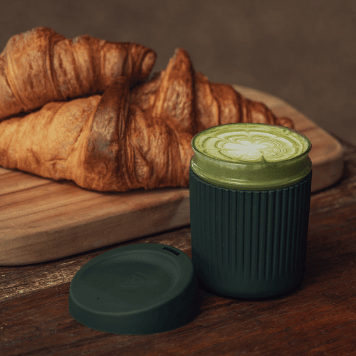 Seed & Sprout Reusable Coffee Cup in Green with a Matcha in it, alongside croissants