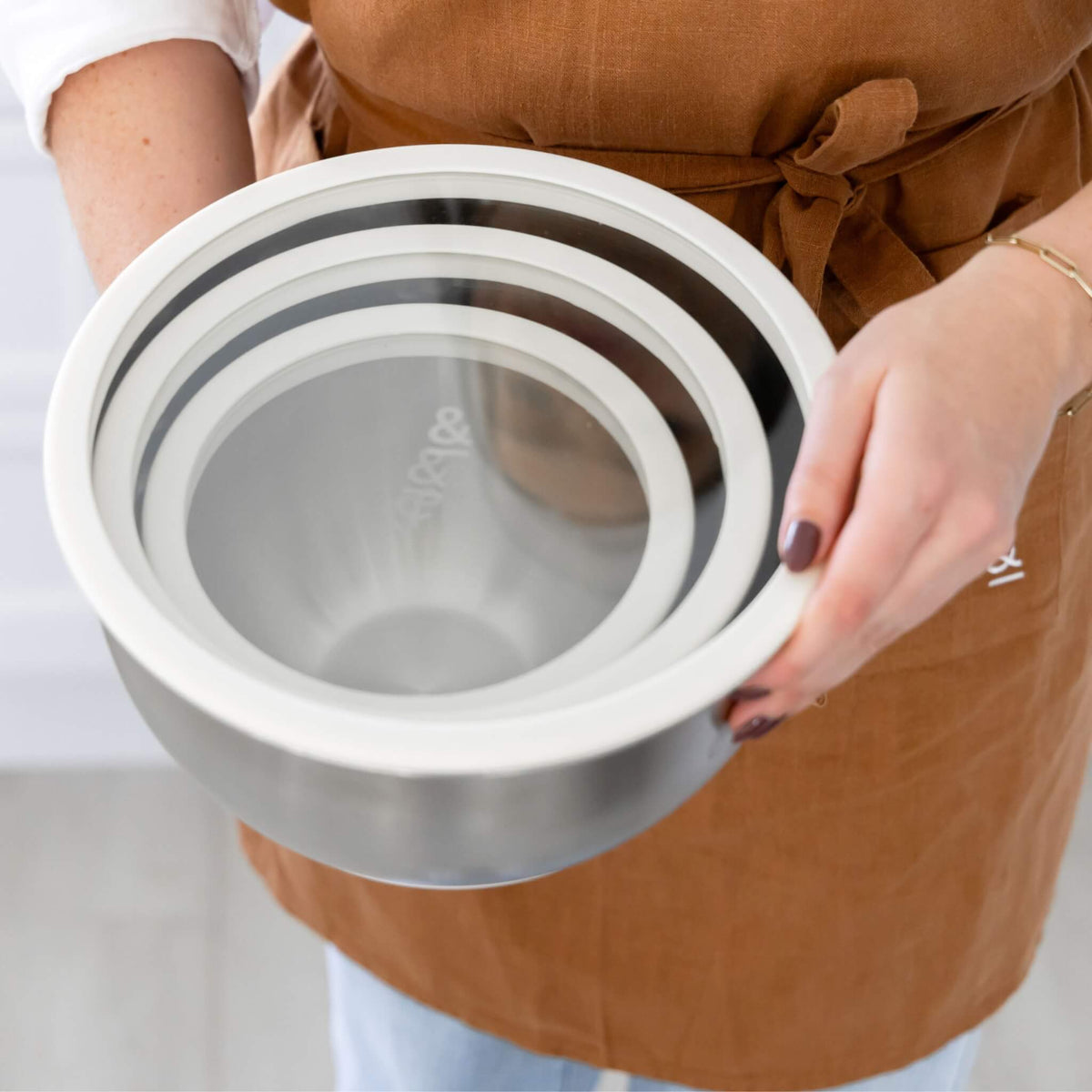 Close-up of the three stainless steel mixing bowls nested together, held from below to show all three sizes fitting compactly inside one another, with white silicone rims visible
