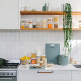 a countertop and shelf showing various kitchen staples from a green scrap bin, green chopping boards and glass food jars