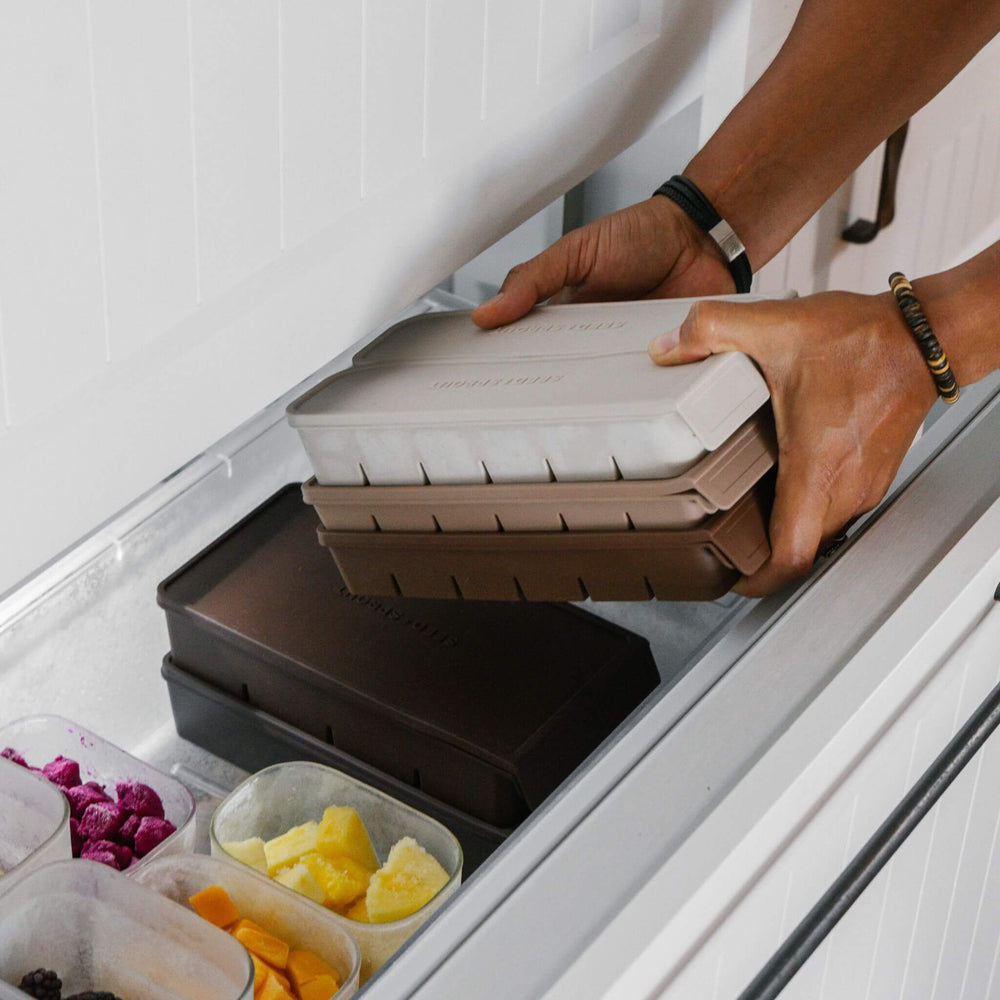 Stacked Seed & Sprout freezer trays with lids sliding into a freezer drawer