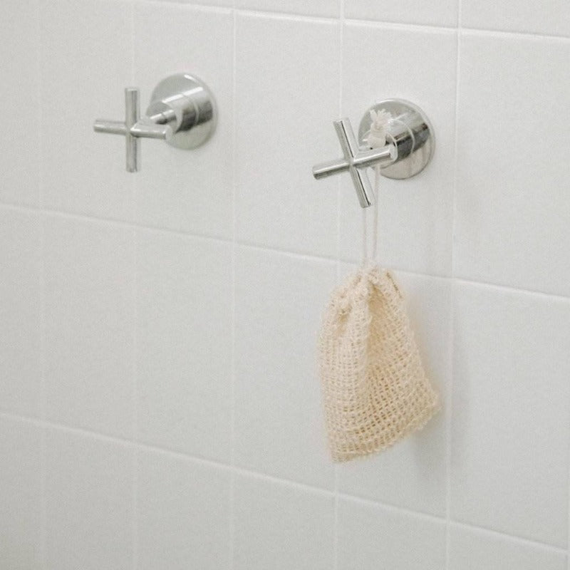 a scrubbing soap bar bag hanging from a shower knob with the drawstring pulled close